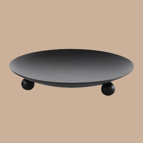 A minimalist black round, iron candle stand with three small spherical feet, shown against a solid beige background.