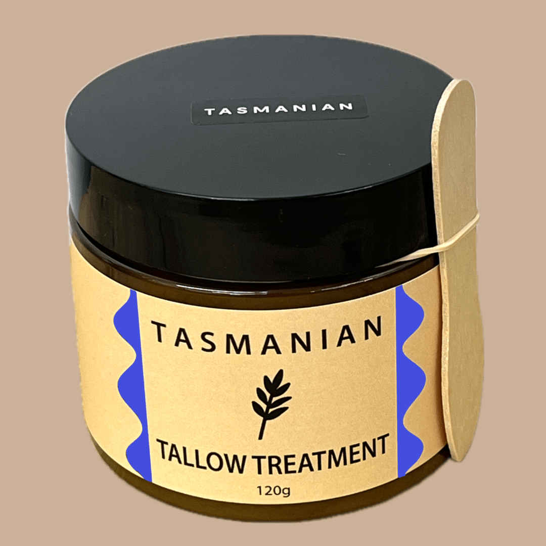 A tub of Tasmanian Tallow Treatment with a black lid and a buff paper label featuring purple accents, shown on a solid beige background.