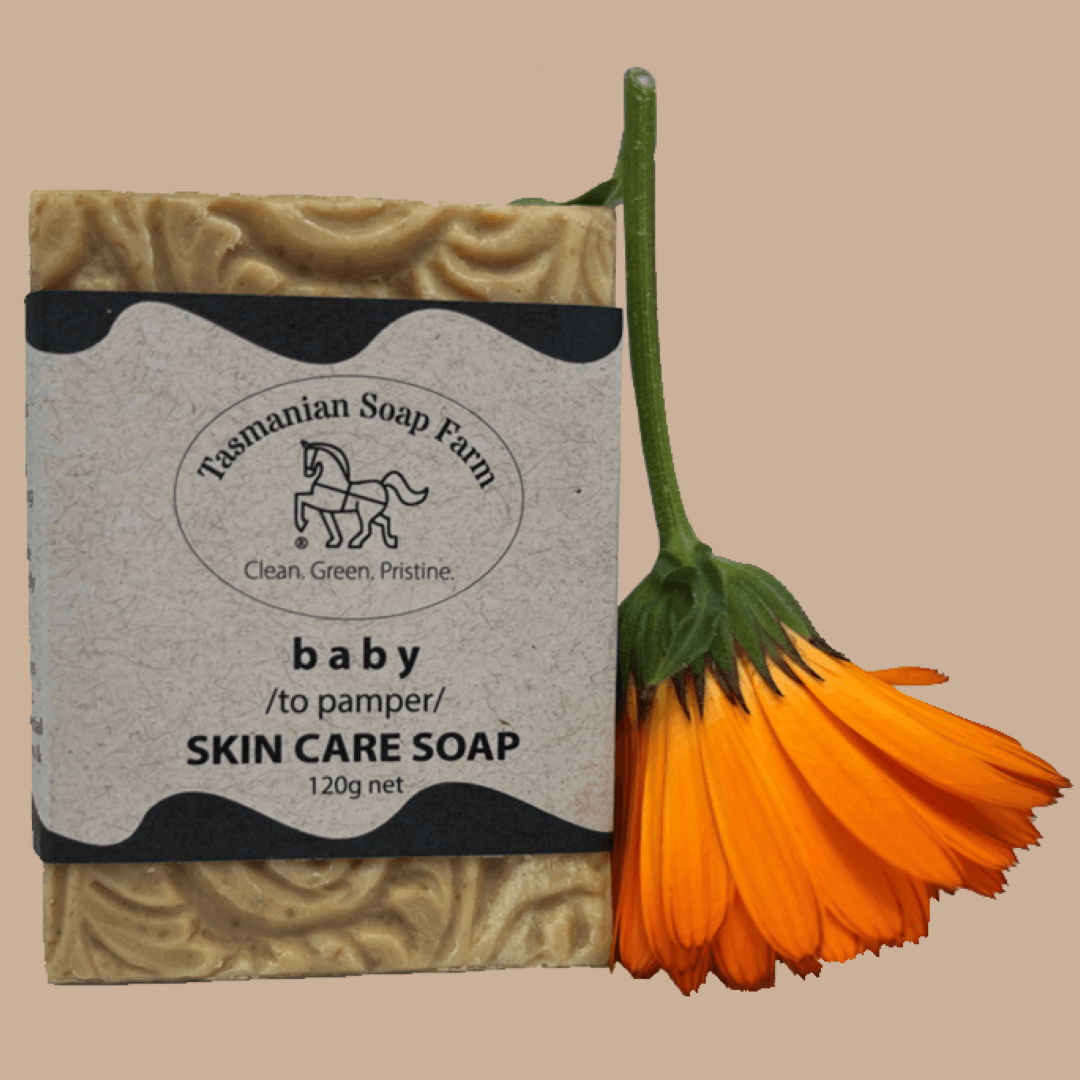 A bar of Tasmanian Soap Farm baby skin care soap next to an orange calendula flower, set against a solid beige background.