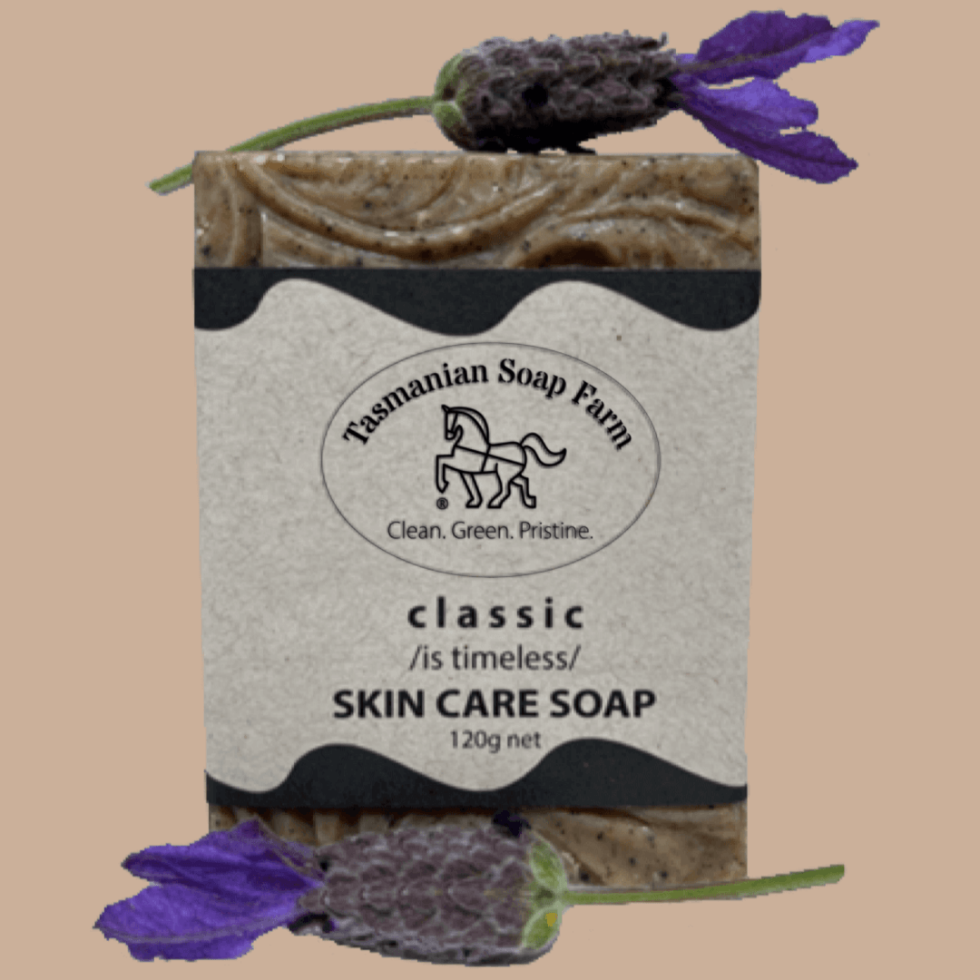 A bar of Tasmanian Soap Farm classic skin care soap with a beige paper label, styled with fresh purple lavender flowers on a solid beige background.