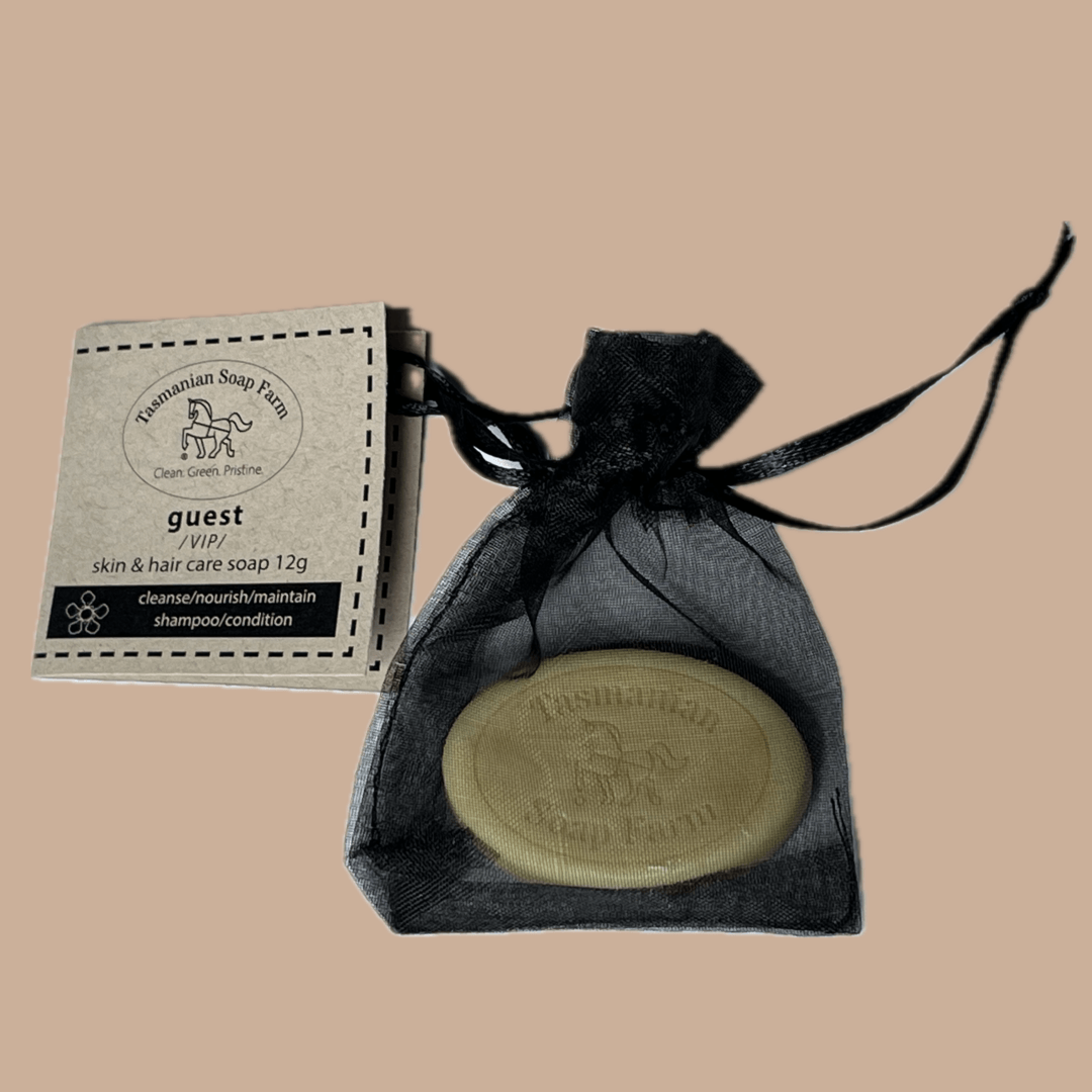 A 12g oval bar of Tasmanian Soap Farm guest skin and hair care soap, displayed next to its paper packaging label and inside a black drawstring pouch.