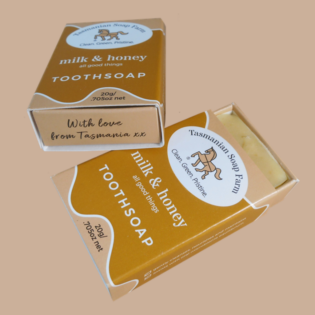 Two boxes of Tasmanian Soap Farm 'milk & honey' toothsoap shown on a solid beige background, with one box open to reveal the pale yellow soap  inside.