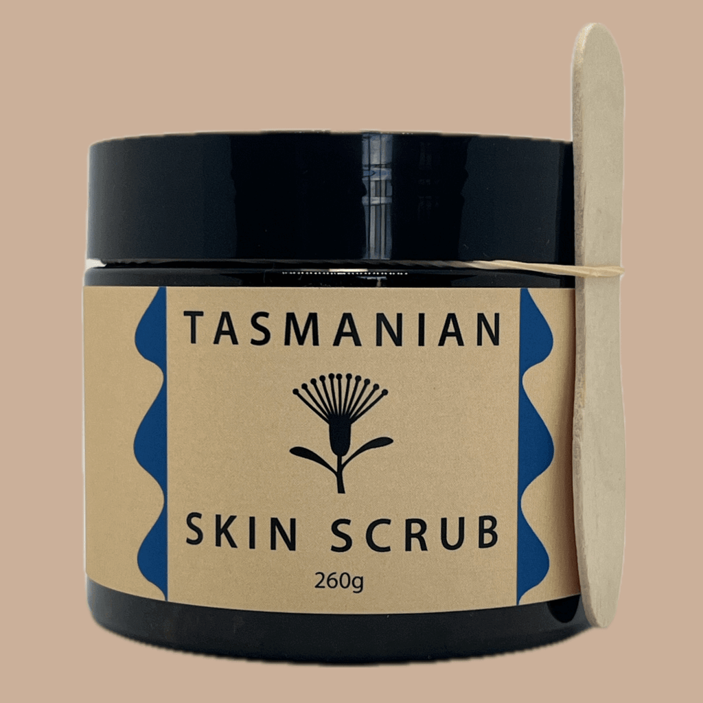 A tub of Tasmanian Skin Scrub with a kraft paper label and a wooden paddle tied to the side, set against a solid beige background.