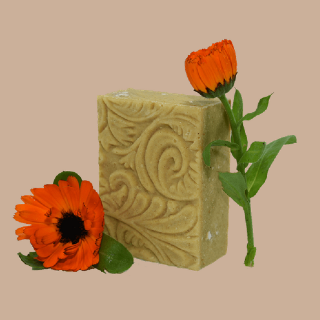 An embossed bar of Tasmanian Soap Farm baby soap styled with two orange calendula flowers on a solid beige background.