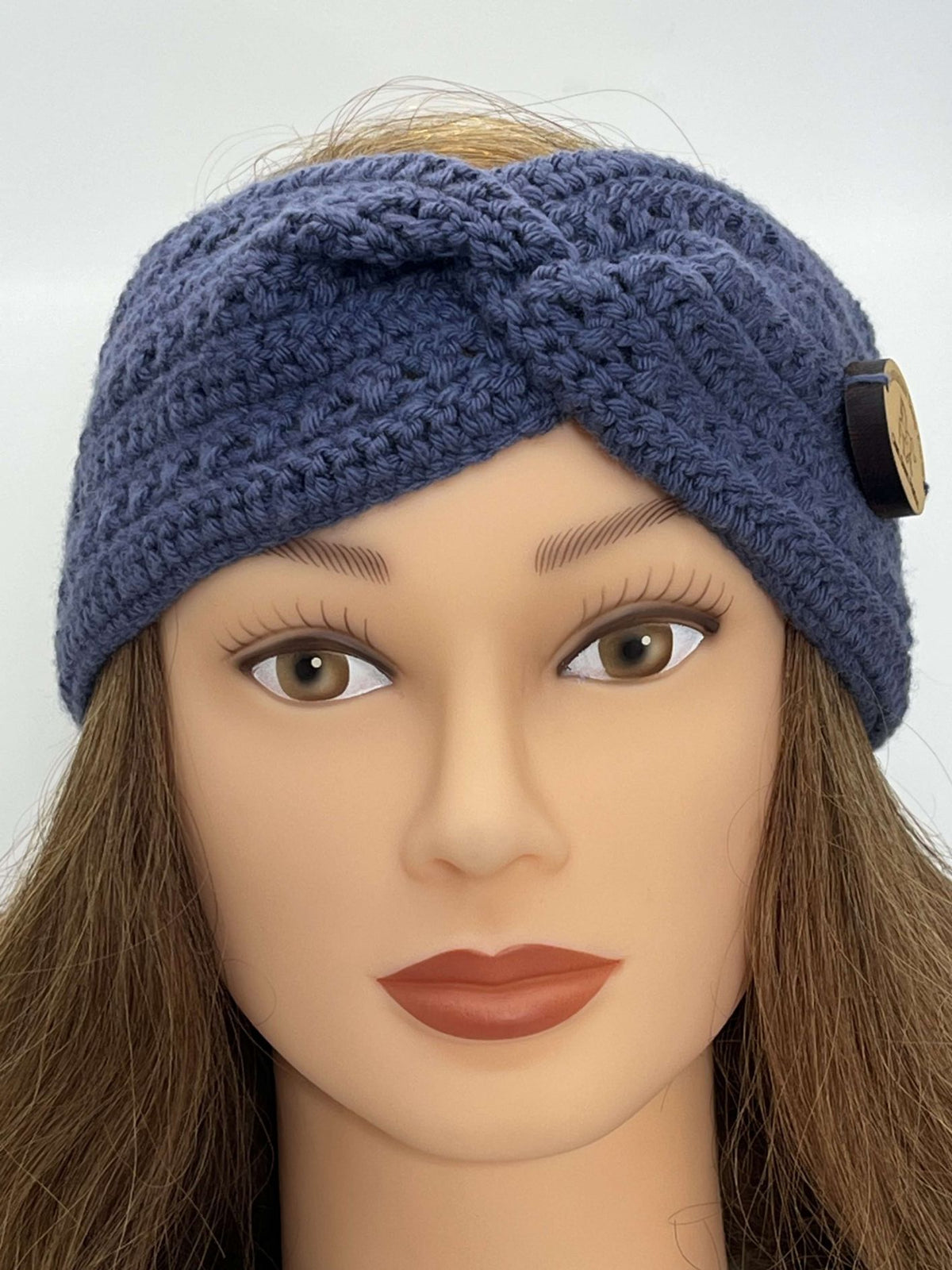 A French blue crocheted headband with a twisted front detail and a decorative gold button accent, displayed on a mannequin head with brown hair against a light gray background.