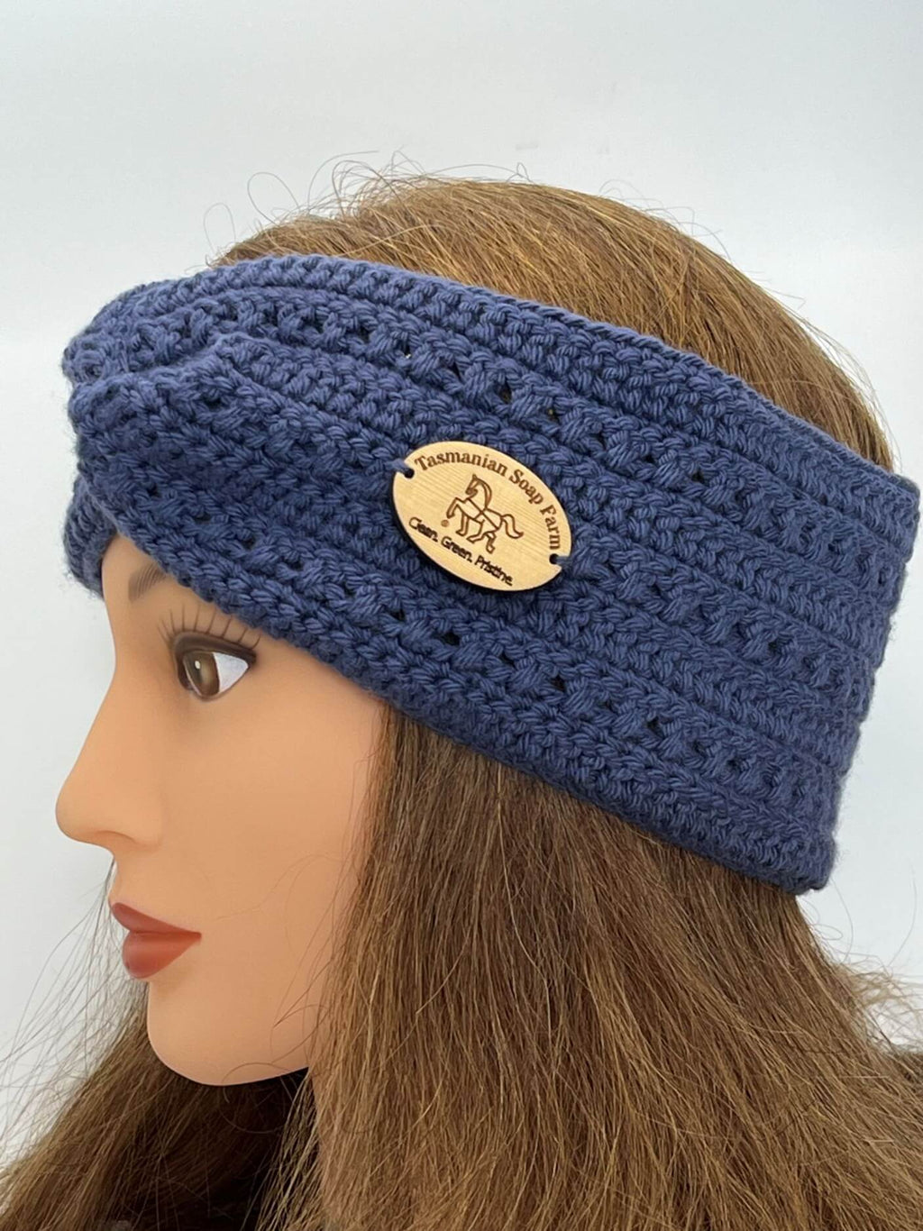 A French blue crocheted headband with a wooden brand plaque, displayed on a mannequin head with long light brown hair against a plain light grey background.