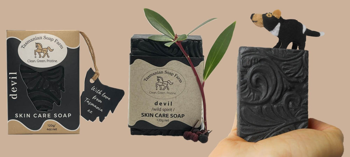 Three views of devil Skin Care Soap by Tasmanian Soap Farm: the retail box on the left, the wrapped soap bar in the centre with a green stem and red pepperberries and an unwrapped dark carved soap bar held in a hand on the right.