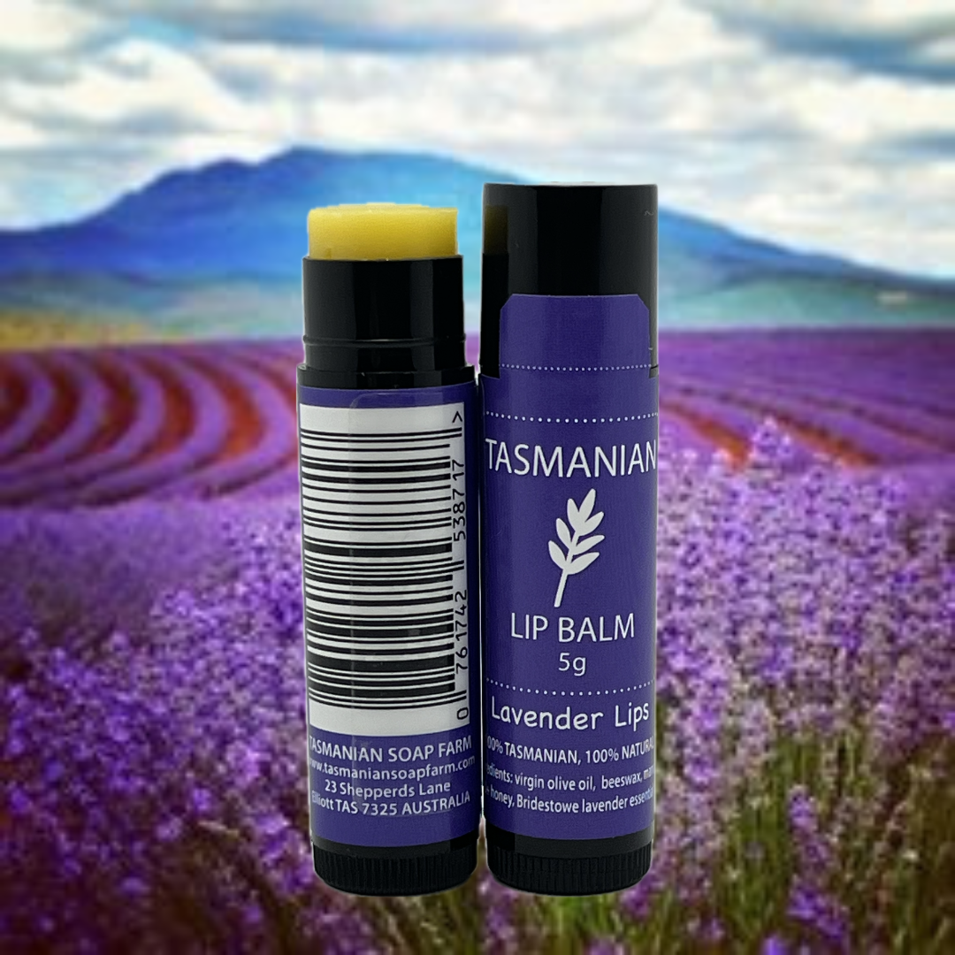 Two tubes of Tasmanian Soap Farm lavender lip balm shown against a scenic background of a purple lavender field and distant mountains. One tube is open, revealing yellow balm, and the other is closed with a purple label.