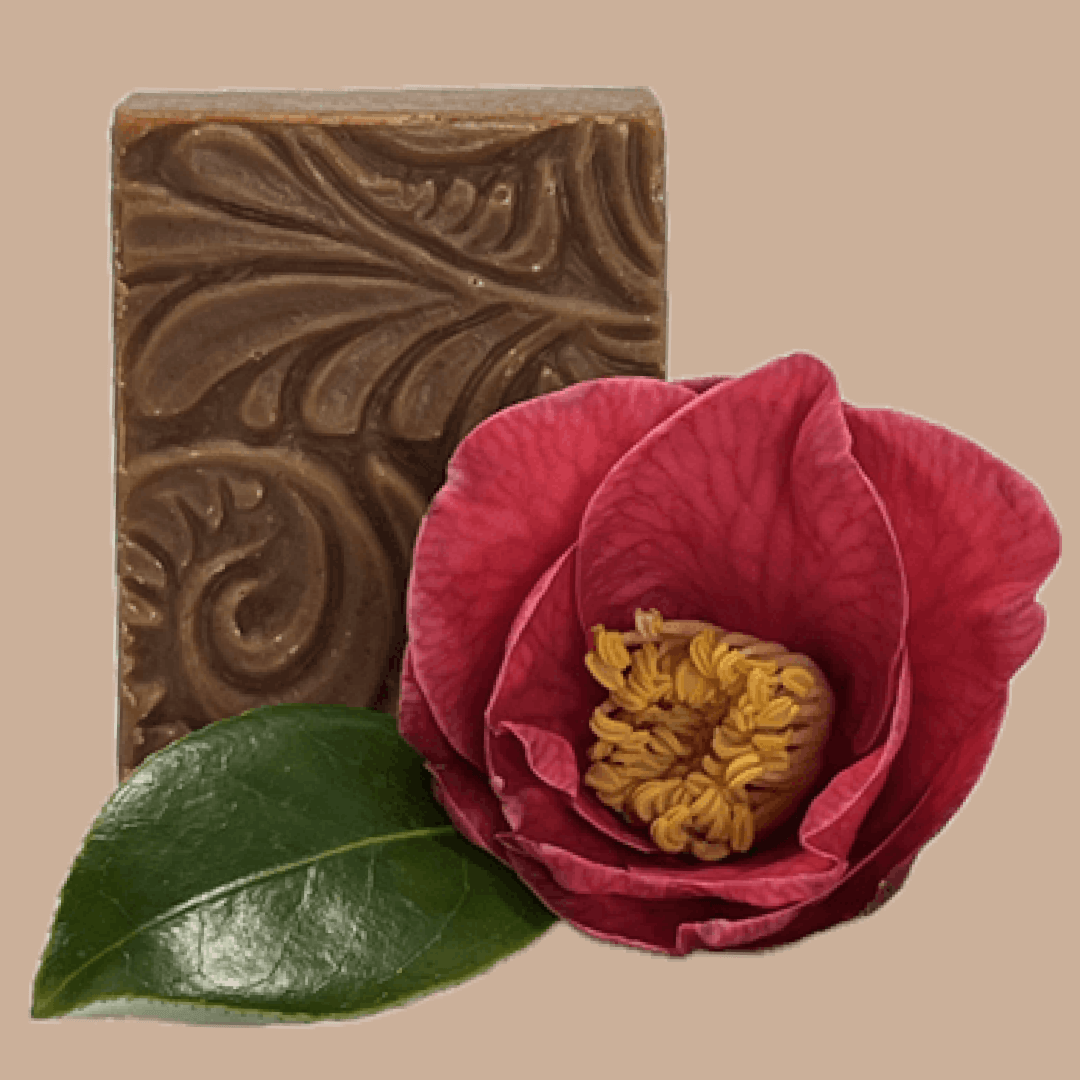 An embossed rectangular bar of Tasmanian Soap Farm rosy soap in a warm brownish-gold tone, shown with a bright pink flower overlay in the lower right corner against a solid beige background.