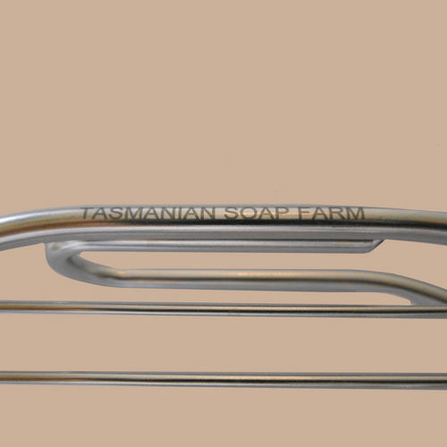 Close-up of a stainless steel soap rack with the engraved brand name 'TASMANIAN SOAP FARM' on a warm beige background.