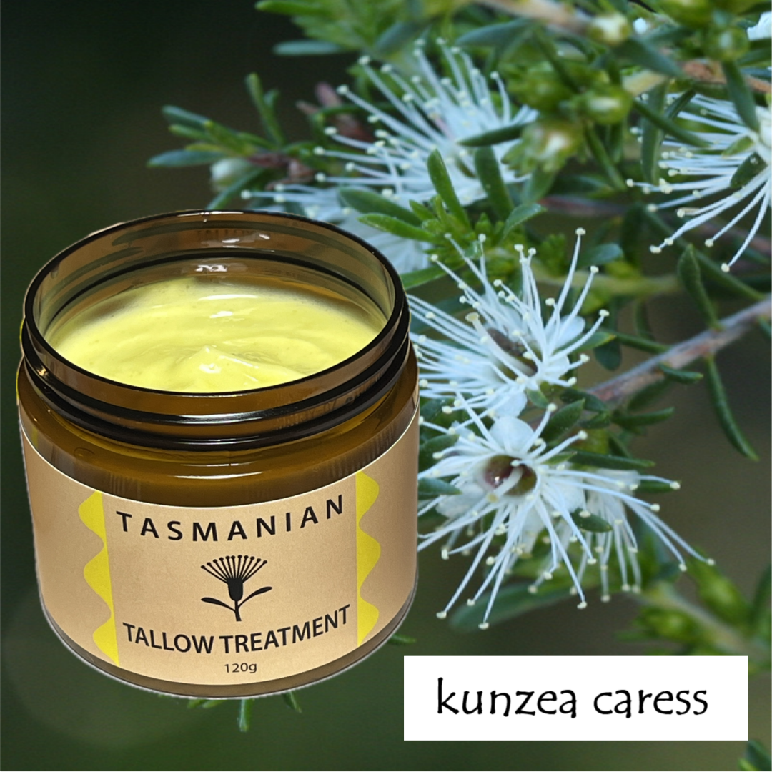An open amber PET pot of Tasmanian Tallow Treatment with pale yellow wax visible inside, placed in front of green leaves and white flowers. A label on the jar reads 'TASMANIAN TALLOW TREATMENT 120g', and a text box at bottom right says 'kunzea caress'.