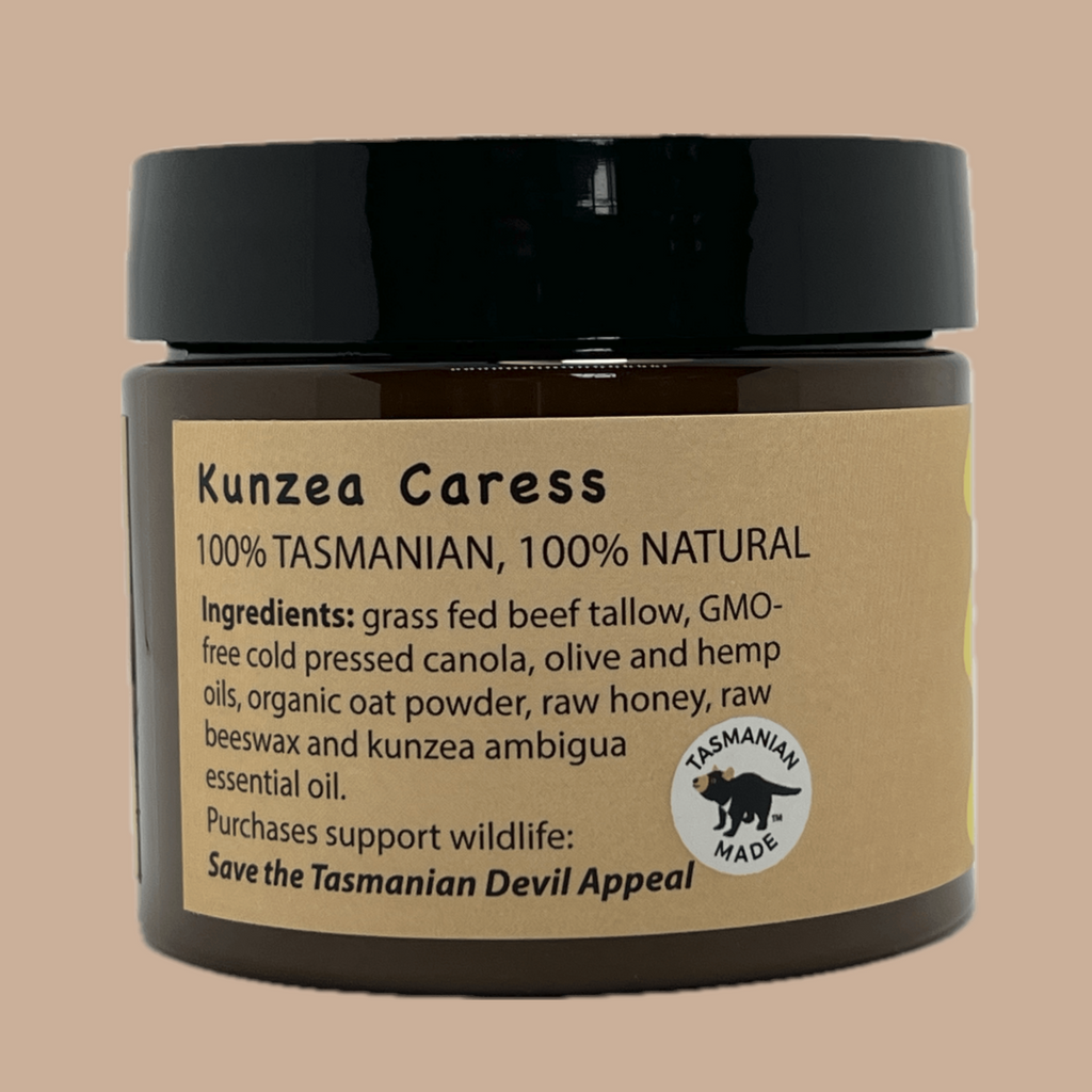 A dark amber PET pot of Kunzea Caress natural tallow product with a black lid and a tan paper label, shown against a solid beige background.