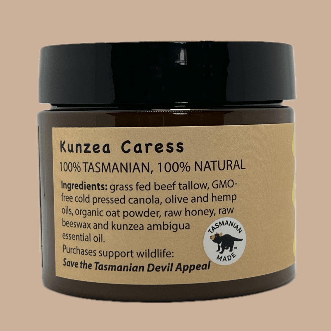 A dark amber PET pot of Kunzea Caress natural tallow product with a black lid and a tan paper label, shown against a solid beige background.