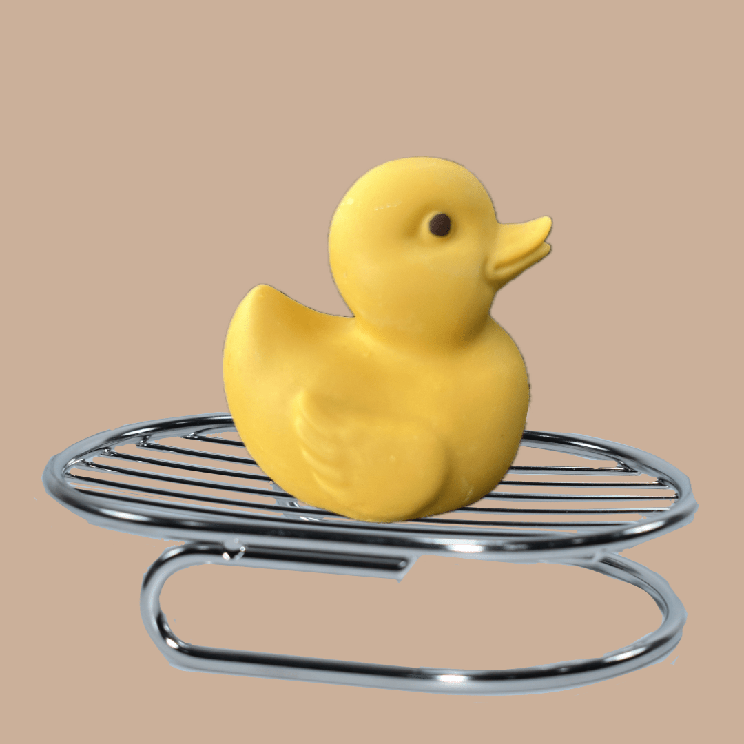 A yellow soap duck toy sitting on an oval  metal soap rack, set against a solid beige background.