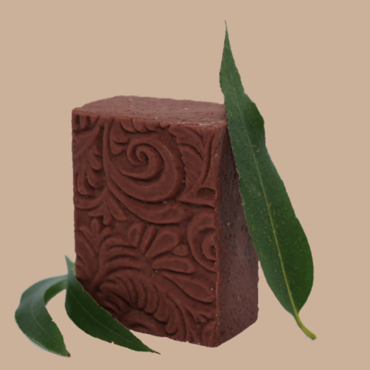 A rectangular bar of dark reddish-brown soap by Tasmanian Soap Farm with embossed floral swirl patterns, styled with green leaves on a solid beige background.