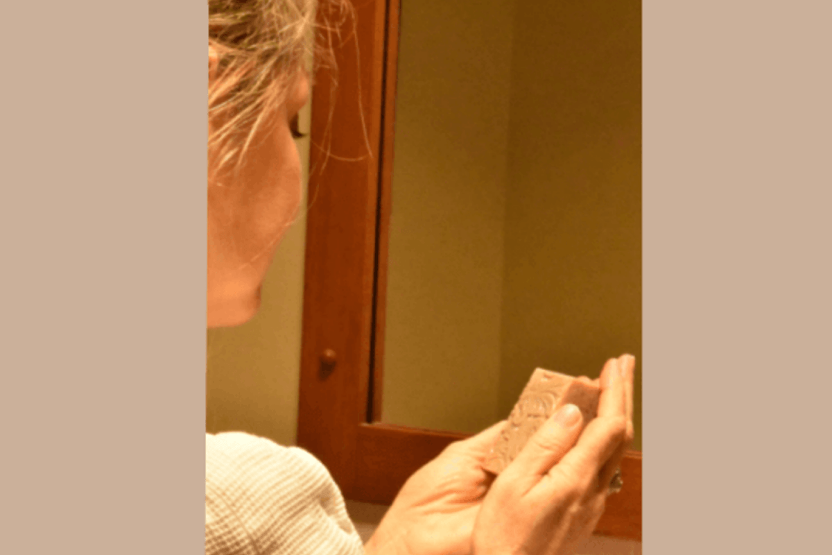 A woman holding a rectangular bar of soap from Tasmanian Soap Farm in front of a mirror.