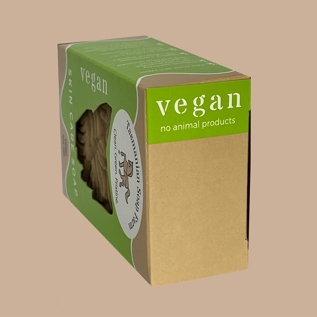 A rectangular cardboard box of vegan skin care soap, by Tasmanian Soap Farm, featuring a green top and side panel with white text, a kraft brown lower panel, and a circular white label. The box is shown at an angle on a solid beige background.