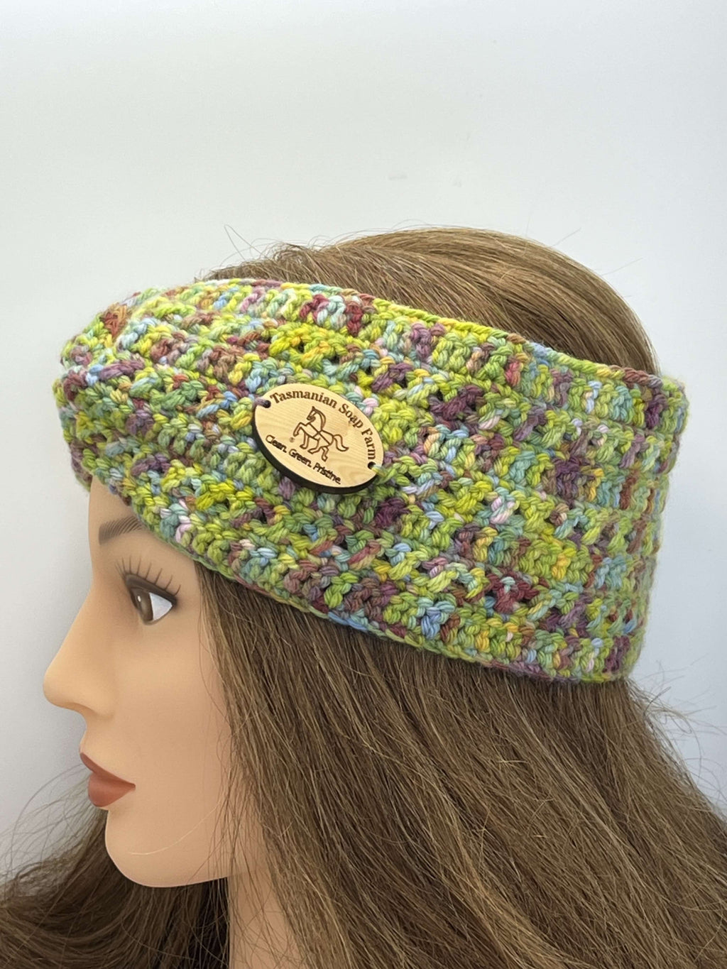 A multicolour crocheted headband by Tasmanian Soap Farm with a wooden brand patch, displayed on a mannequin head with long brown hair against a plain white background.