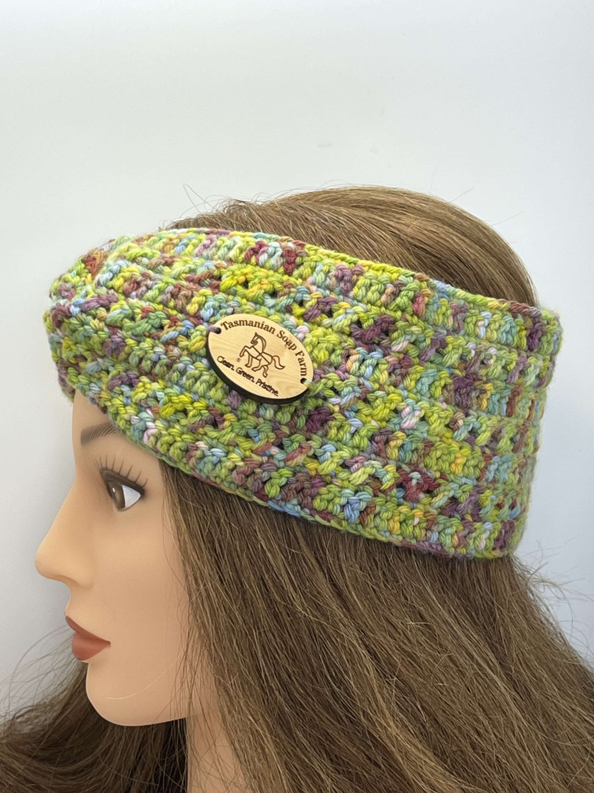 A multicolour crocheted headband by Tasmanian Soap Farm with a wooden brand patch, displayed on a mannequin head with long brown hair against a plain white background.