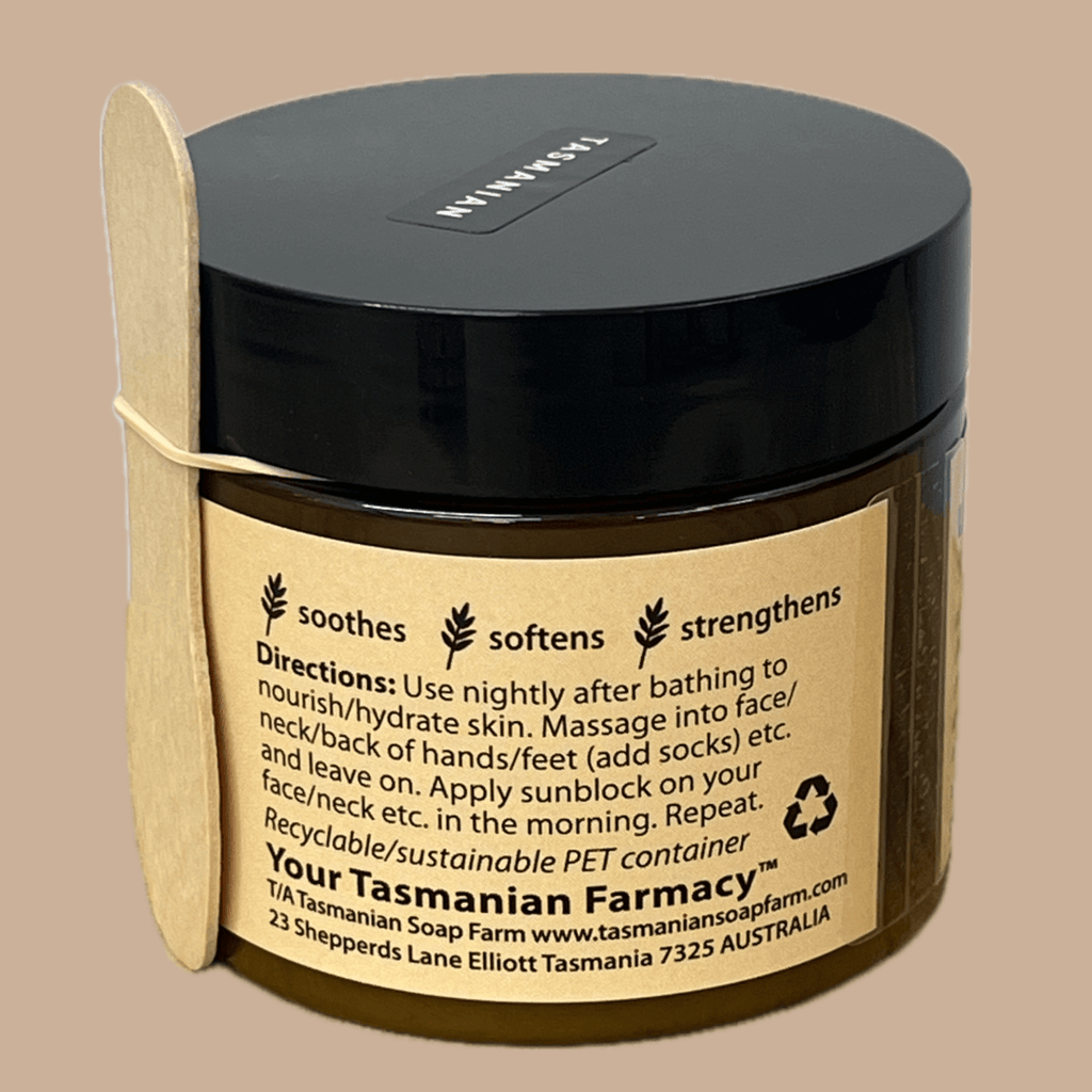 A dark amber jar of Tasmanian Tallow Treatment face and neck cream with a black lid and a light wood spatula resting on its side, set against a solid beige background.