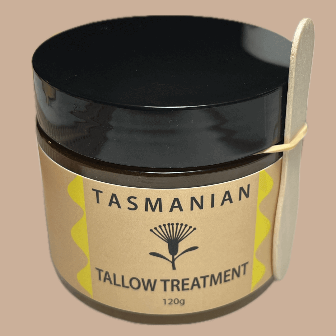 A jar of Tasmanian Tallow Treatment with a black lid and a beige label featuring yellow accents, shown with a wooden spatula on a solid beige background.