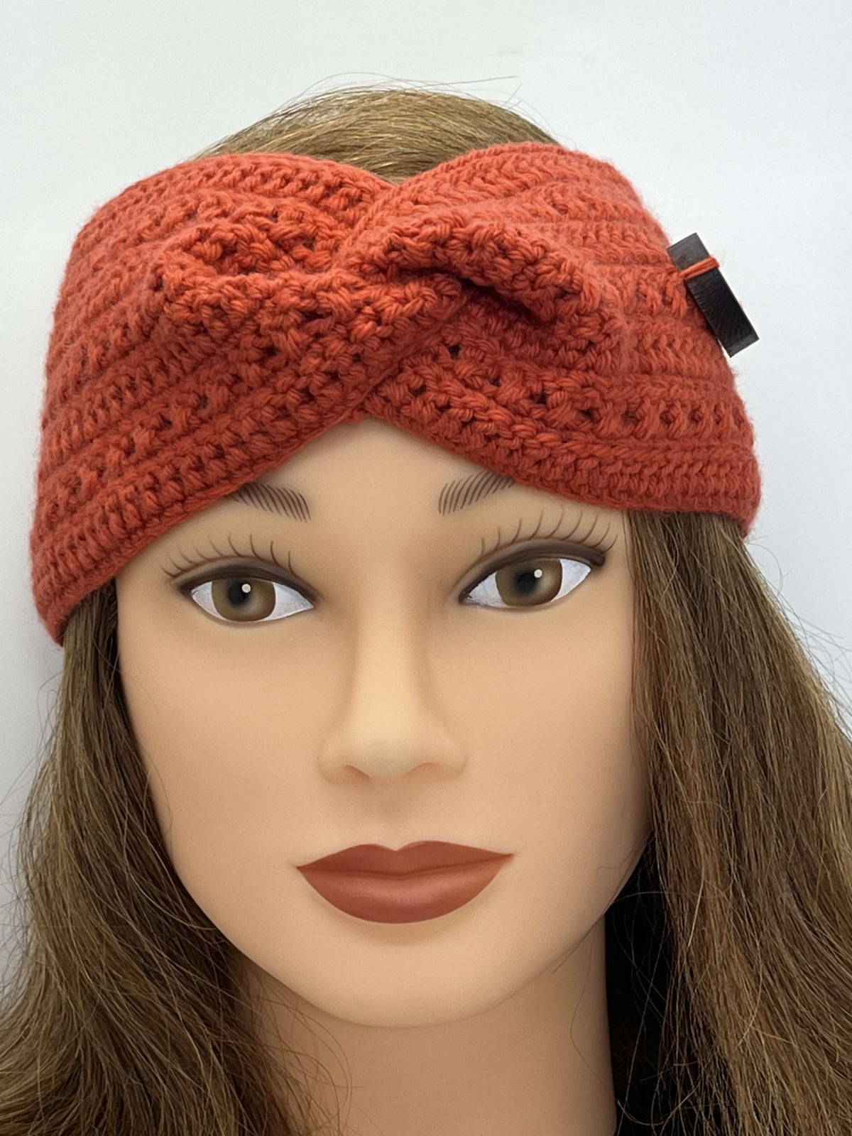 A coral crocheted headband by Tasmanian Soap Farm with a twisted front detail and a small black tag, displayed on a mannequin head with brown hair against a plain white background.