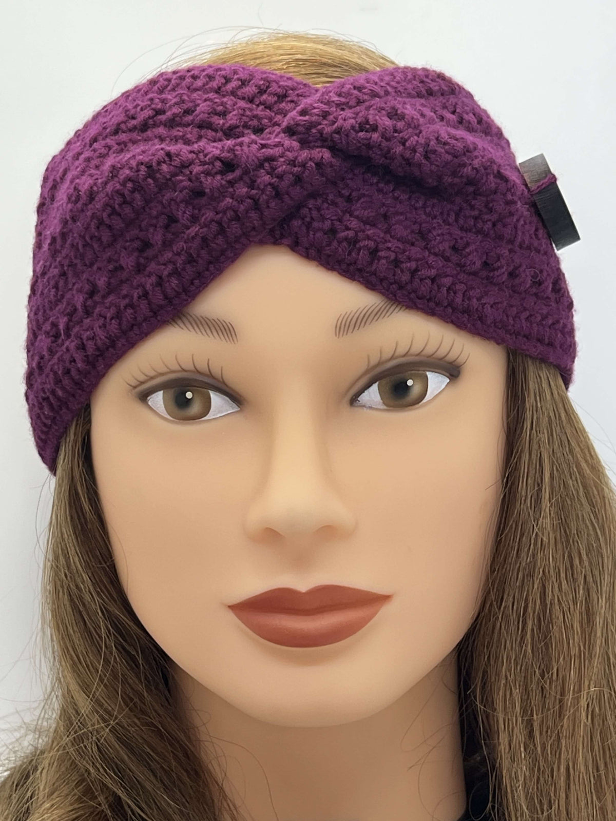 A close-up of a mannequin head wearing a chunky crocheted twist-front headband by Tasmanian Soap Farm in deep plum purple. The mannequin has long light brown hair, and a small black tag is attached to the side of the headband.