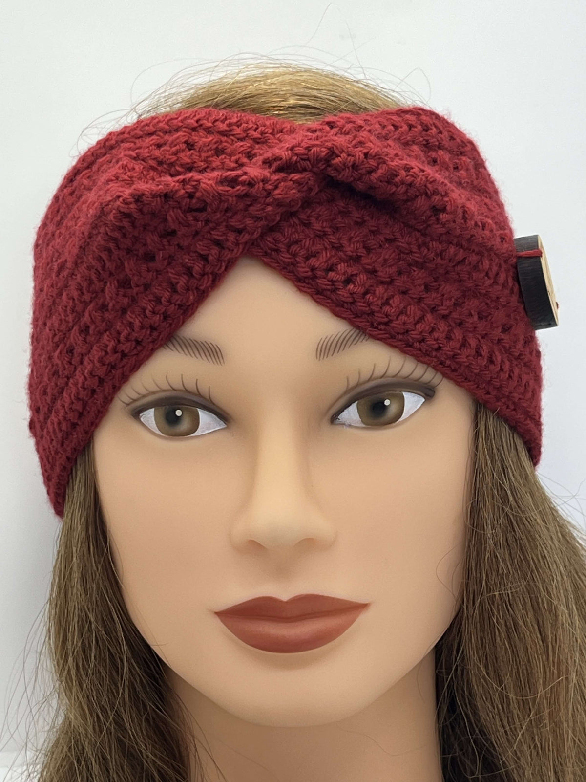 A dark red crocheted twist-front headband by Tasmanian Soap Farm with a small black and gold button closure, shown on a mannequin head with brown hair against a plain white background.
