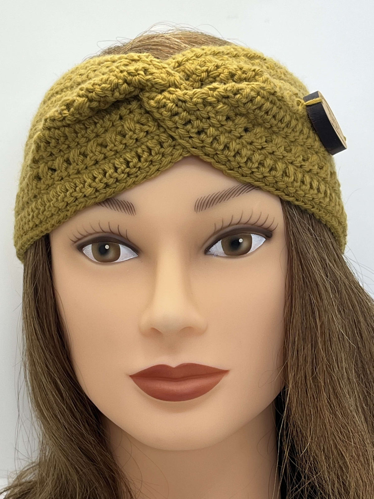 A close-up of a mannequin head wearing a Tasmanian Soap Farm chunky crocheted twisted headband in mustard with a timber button on the side.