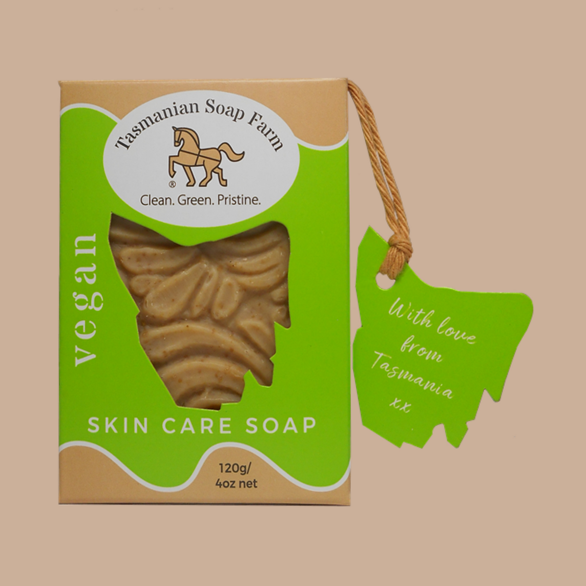 A boxed vegan skin care soap from Tasmanian Soap Farm, shown on a plain beige background. The kraft-paper style box has a bright green front panel with a clear window in the shape of a map of Tasmania, revealing the soap inside, plus a green hanging tag with handwritten text.