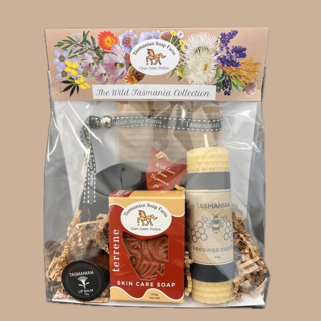 Tasmanian Soap Farm's 'The Wild Tasmania Collection' gift set in a clear cello bag, containing a soap bar, beeswax candle, skin care soap, and accessories on a solid buff background.